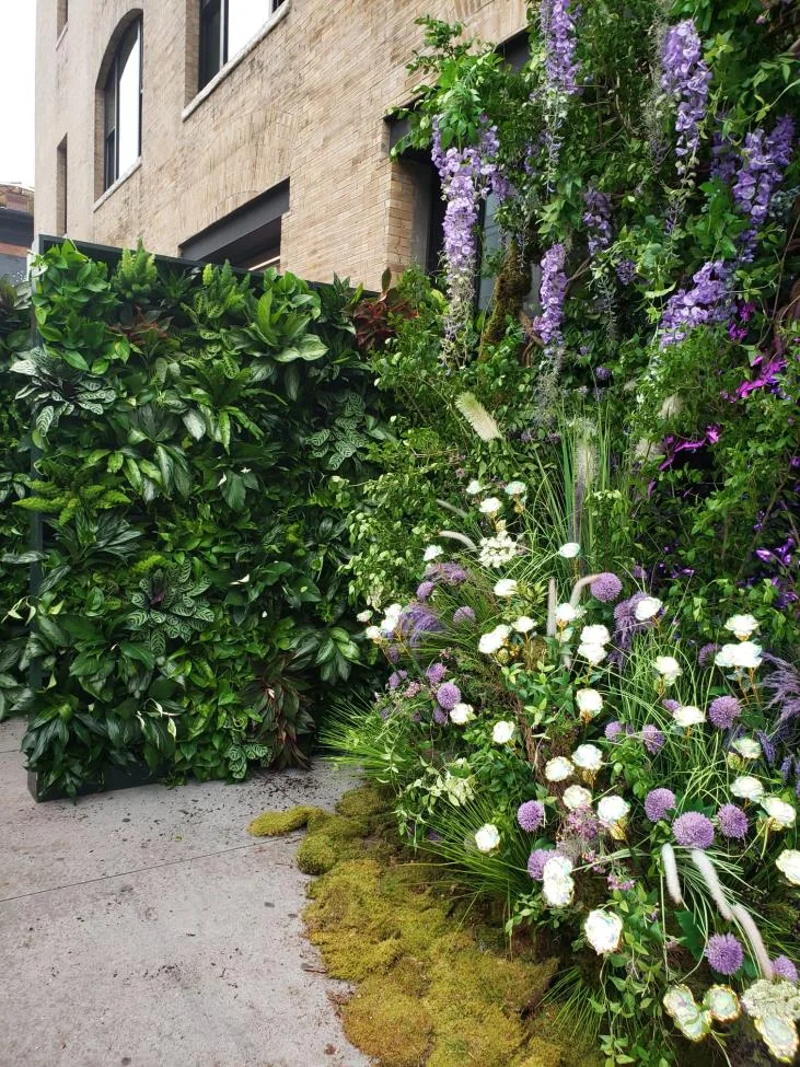 Flowering greenery and a living wall frame a garden-like entrance.