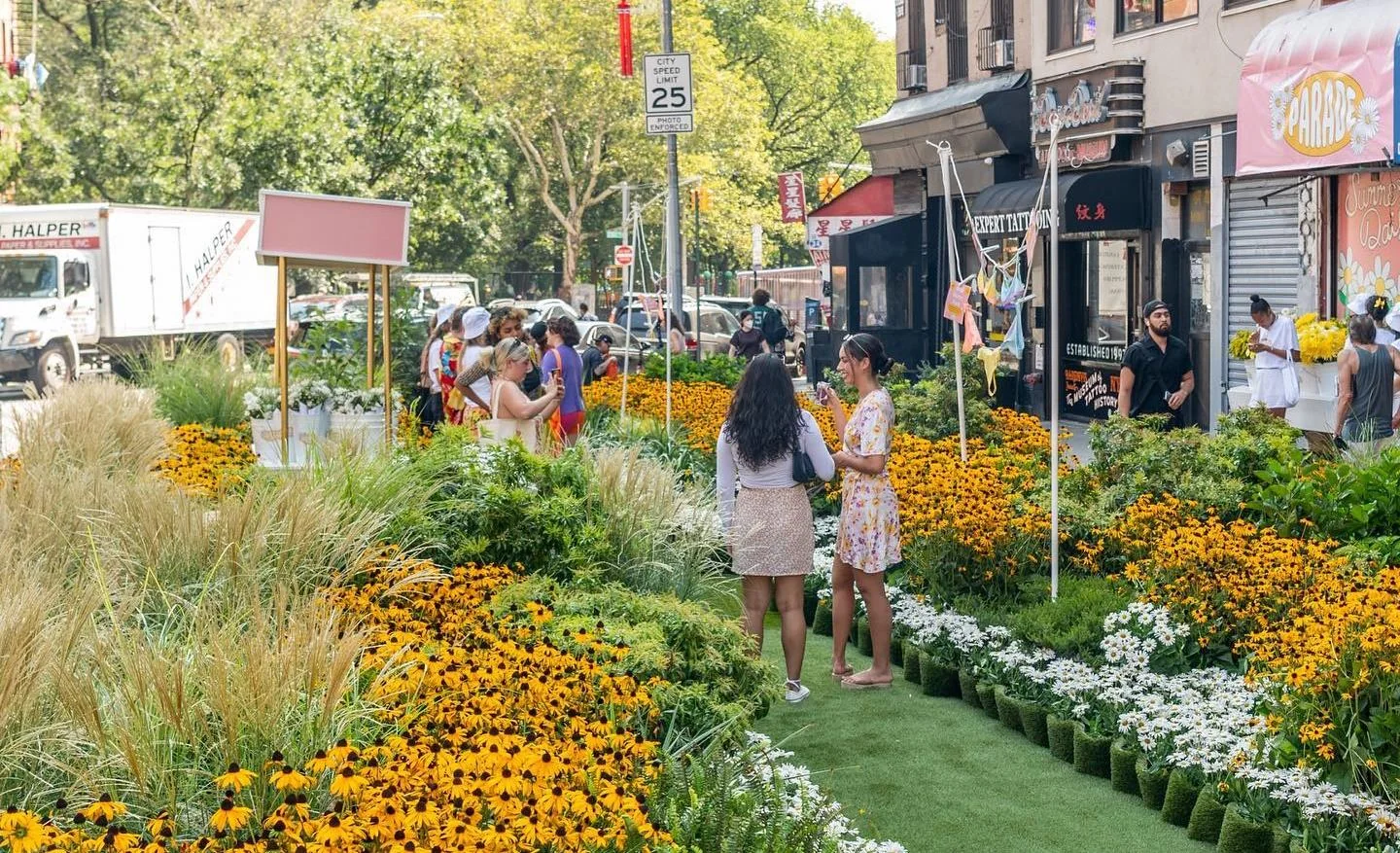 A street transformed by flowering plants, grasses, and a green walking path.